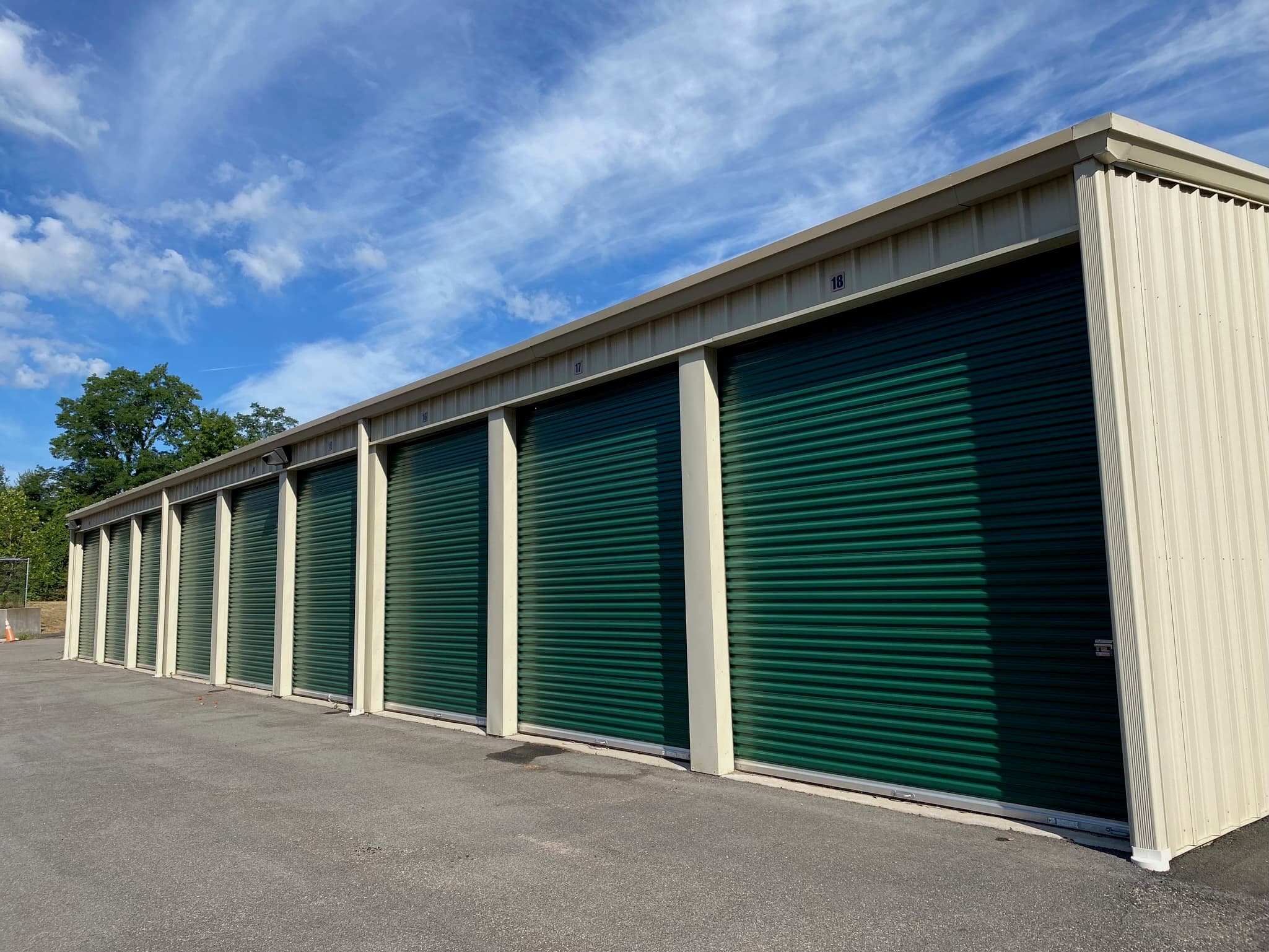 A row of drive-up storage units with green roll-up doors on a paved apron