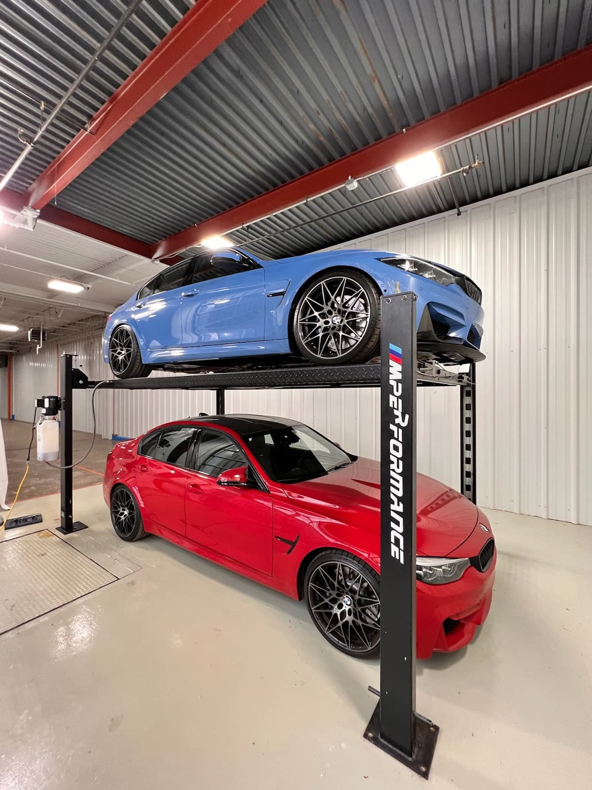Two cars stacked on a lift inside the vehicle building